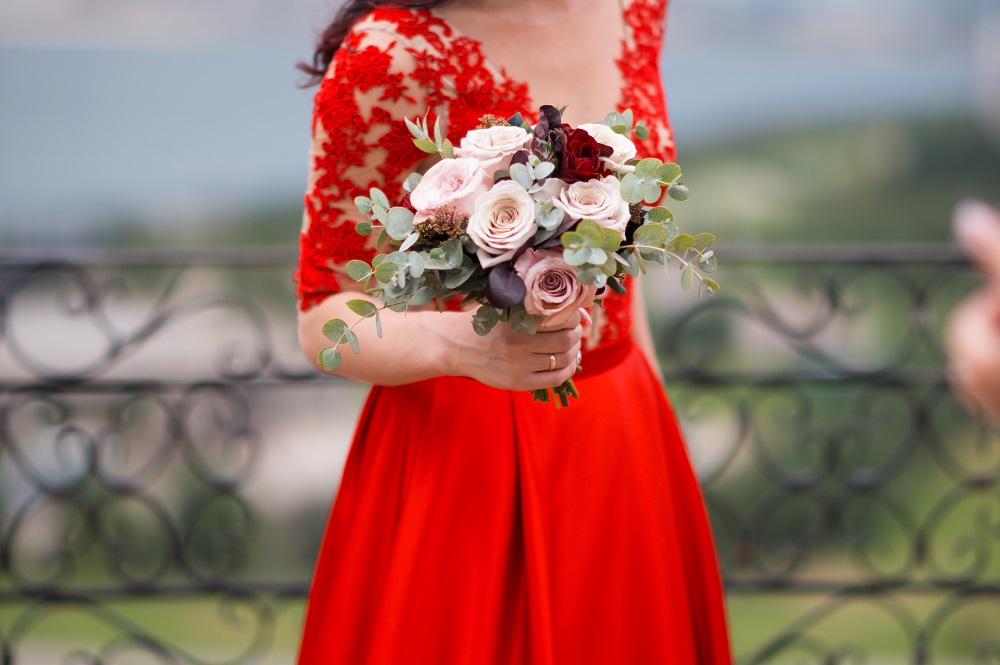Czerwona suknia ślubna. Panna młoda w czerwonej sukni trzyma bukiet pięknych kwiatów.