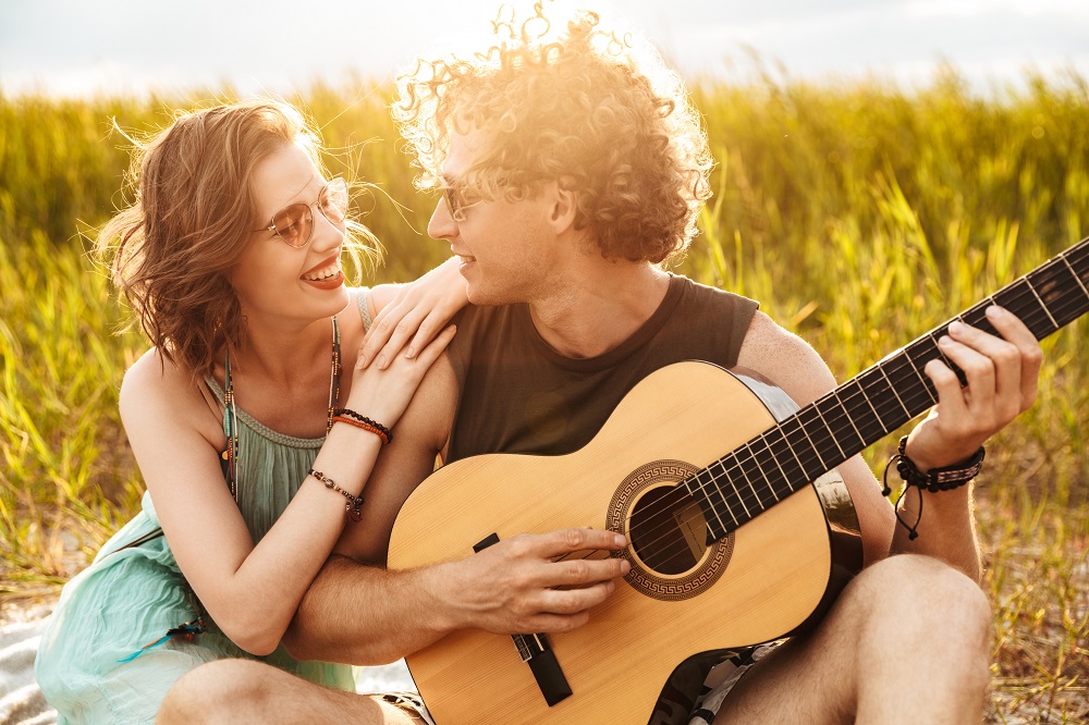 piosenka na zaręczyny - mężczyzna siedzi na łące ze swoją kobietą i gra jej na gitarze