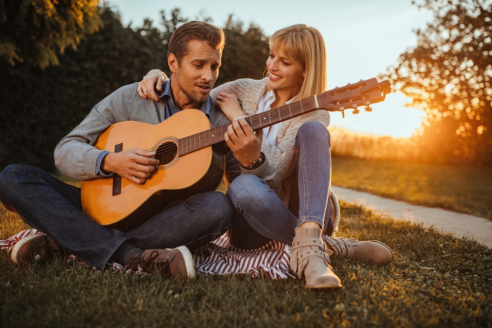 piosenka na zaręczyny - mężczyzna gra na gitarze swojej ukochanej o zachodzie słońca