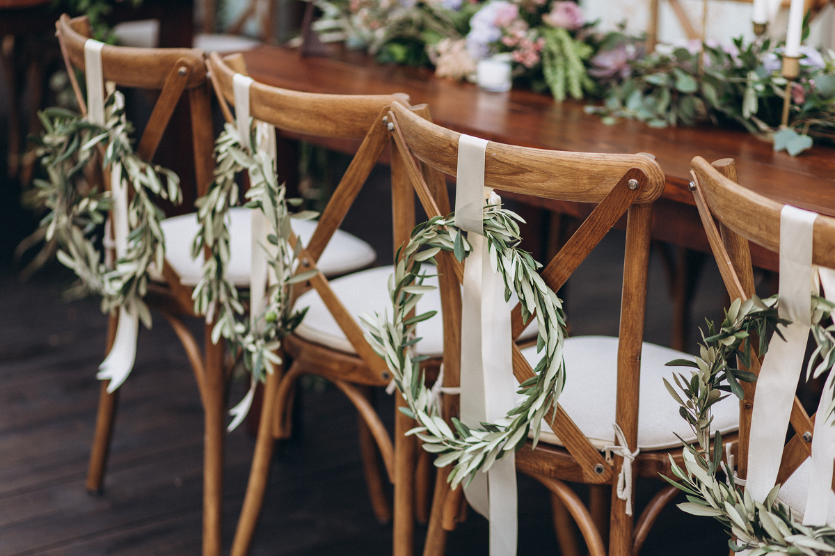 Dekoracja sali weselnej - krzesła ozdobione zielonymi wieńcami