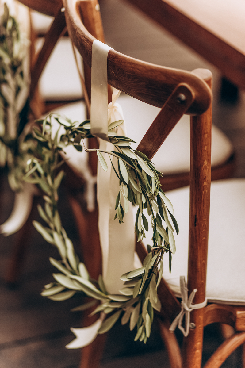 Dekoracja sali weselnej - wieniec z zielonych liści zawieszony na krześle