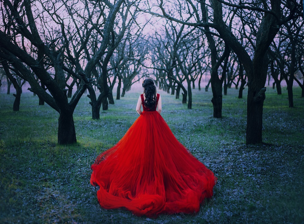 Kolorowe suknie ślubne. Kobieta w długiej, czerwonej sukni w lesie.
