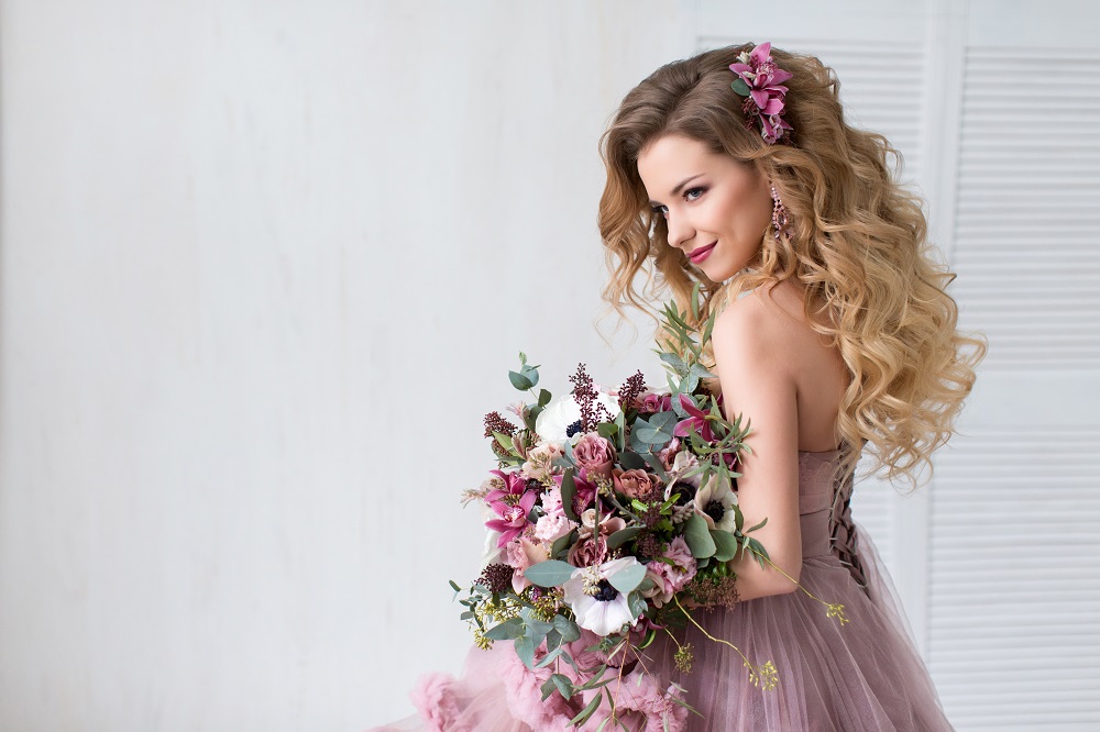 Kolorowe suknie ślubne. Panna młoda w różowej sukni ślubnej trzyma bukiet kwiatów.