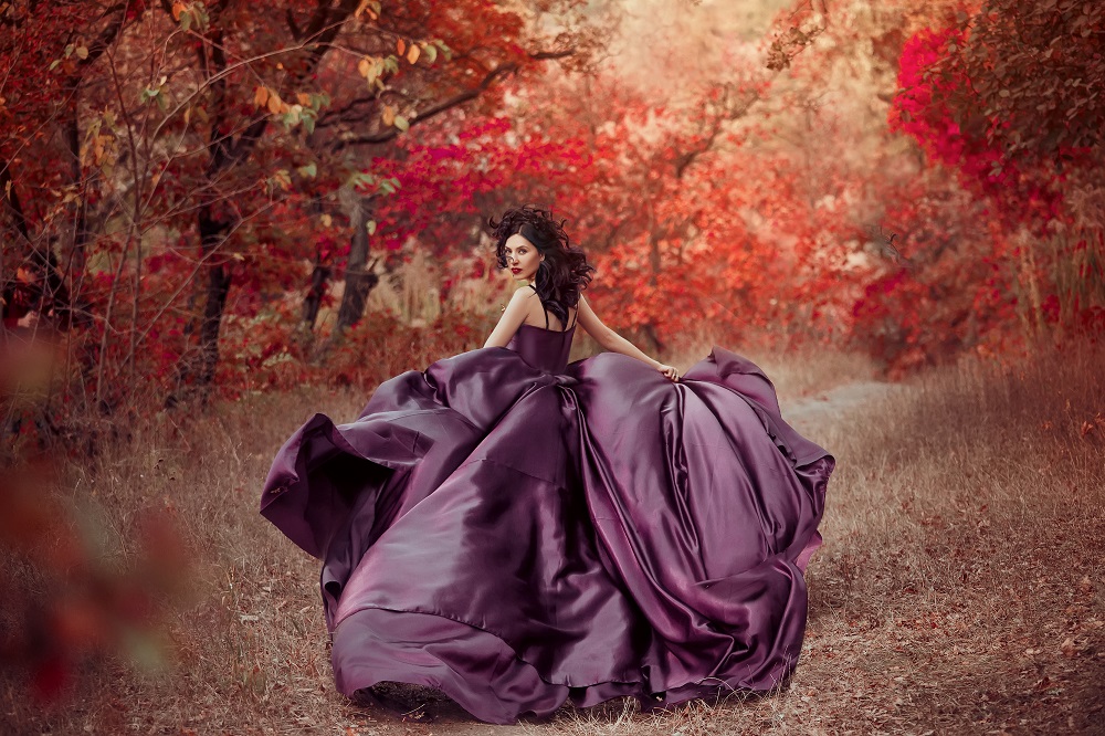 Kolorowe suknie ślubne. Kobieta w długiej, fioletowej sukni na sesji zdjęciowej w lesie.