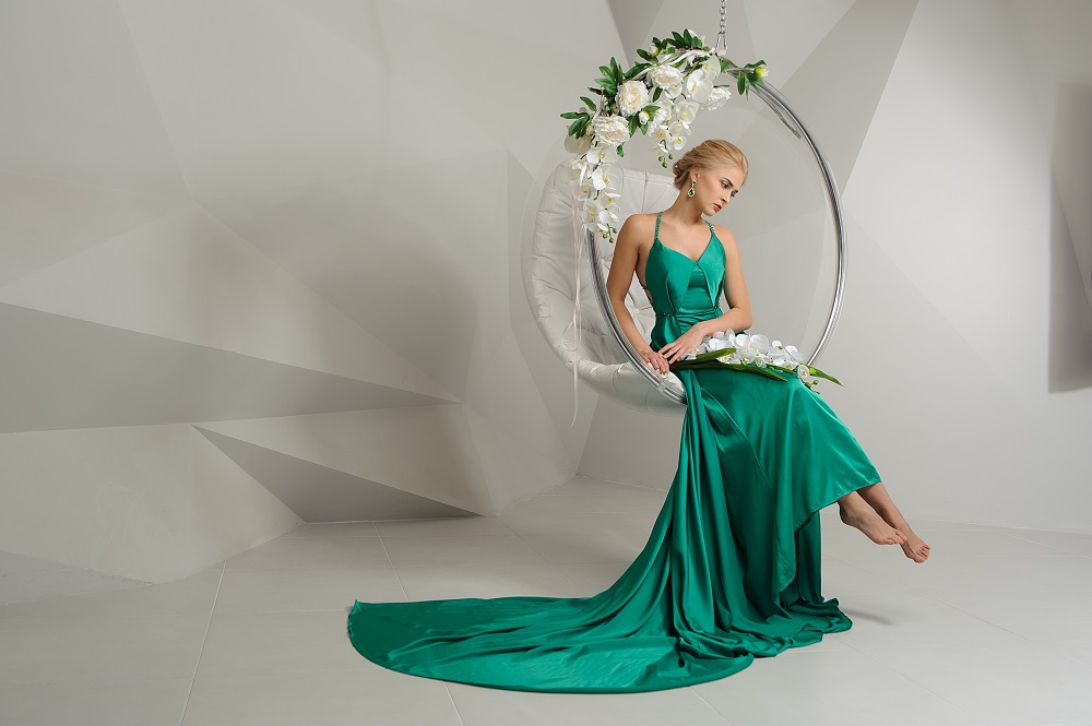 Kolorowe suknie ślubne. Piękna blondynka w zielonej, długiej sukni trzymająca kwiaty.