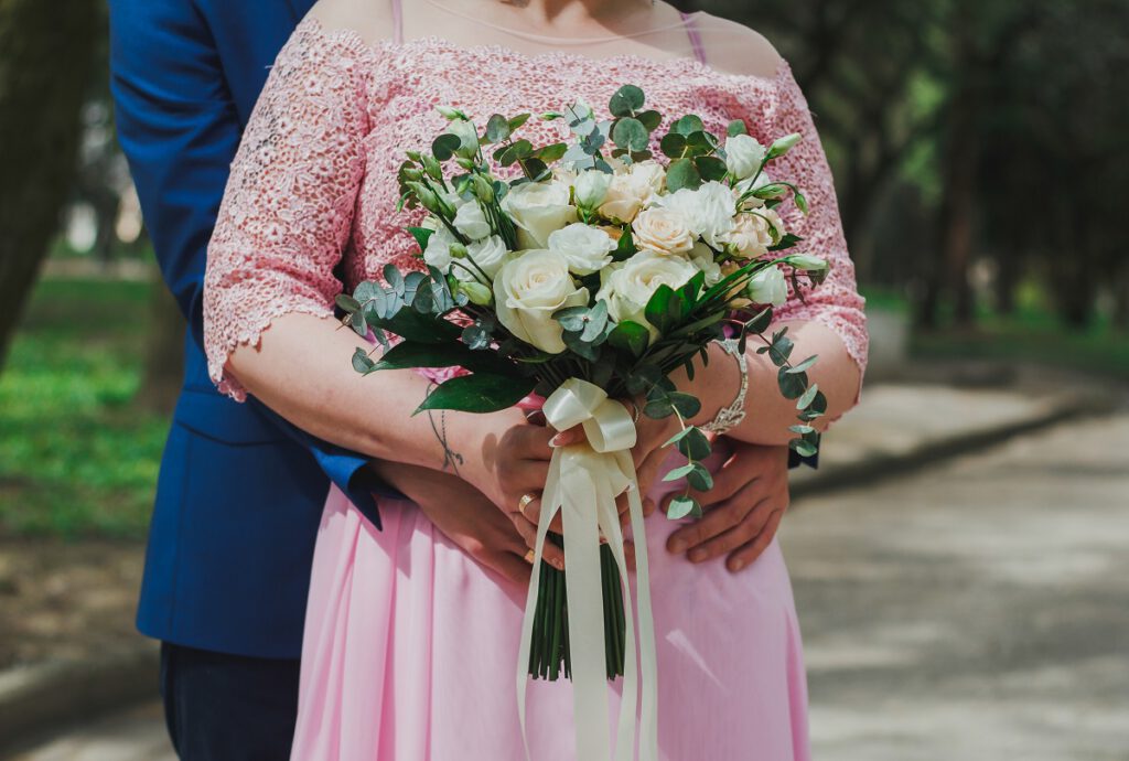 suknie ślubne dla puszystych - panna młoda w różowej sukni ślubnej z bukietem