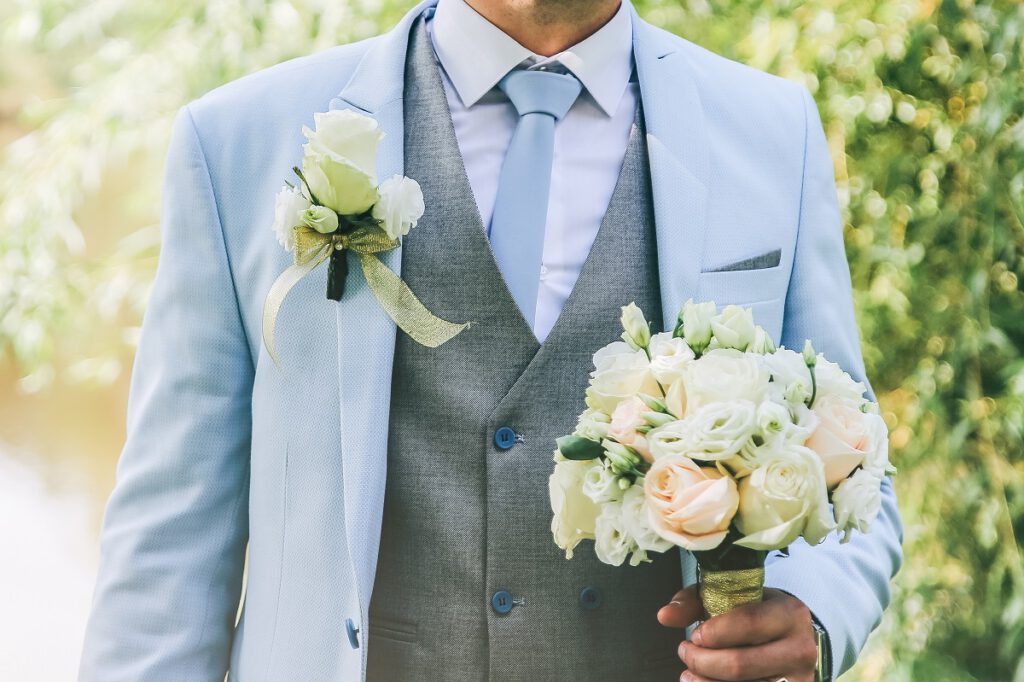 garnitur na wesele - mężczyzna w niebieskim garniturze z bukietem kwiatów
