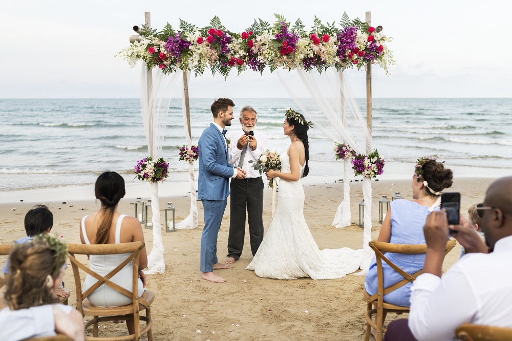 Ślub humanistyczny. Celebrant udzielający ślubu parze młodej na plaży.