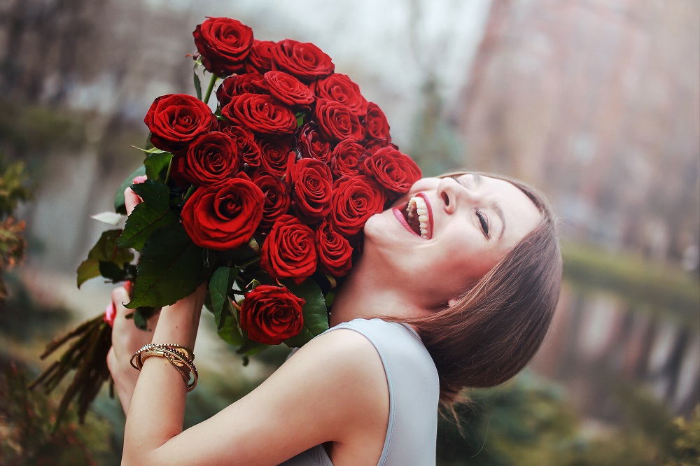 Bukiety ślubne z róż. Uśmiechnięta kobieta trzymająca bukiet czerwonych róż.