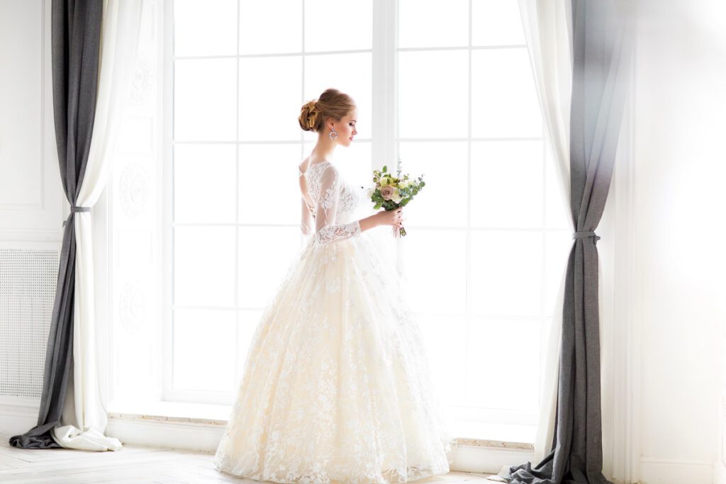 Rodzaje sukien ślubnych - panna młoda w białej sukni przed oknem