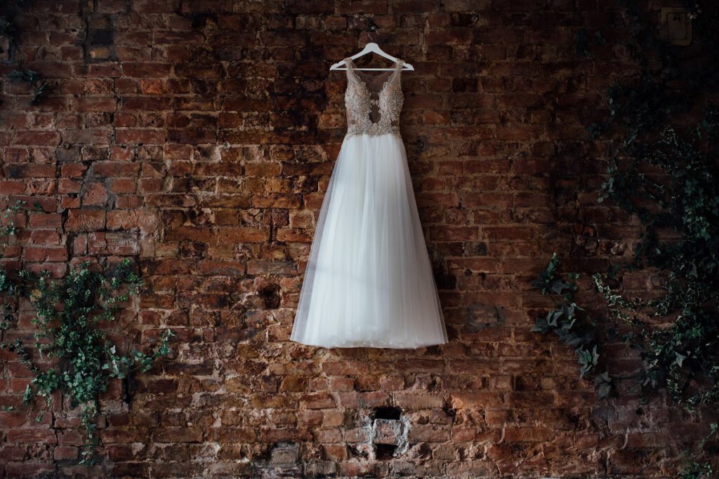 klasyczna suknia ślubna zawieszona na tle ceglanej ściany
