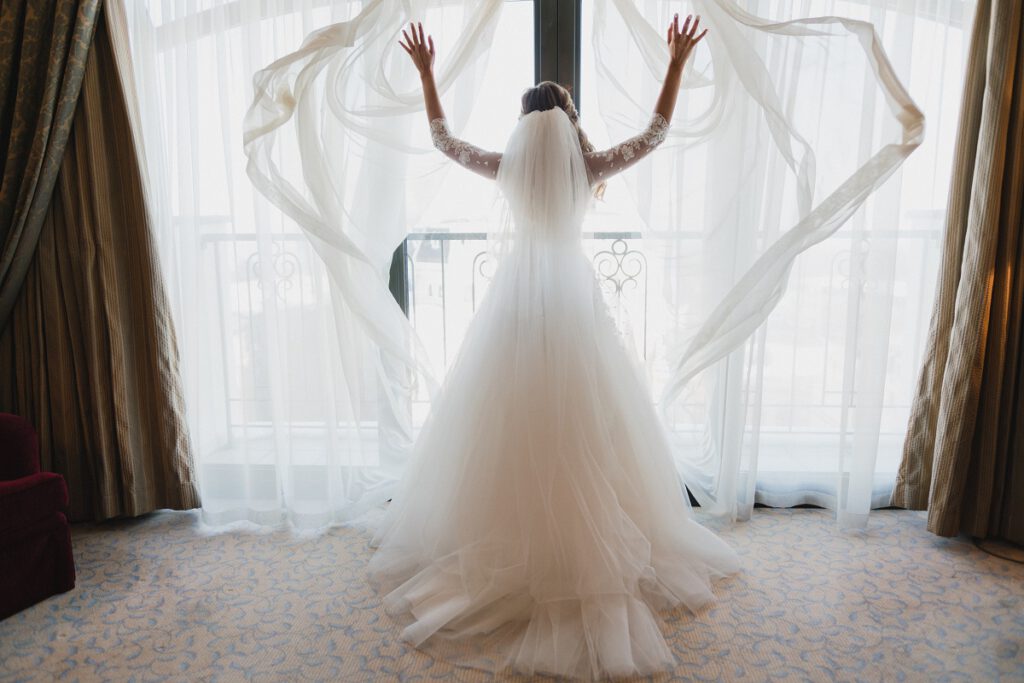 klasyczna suknia ślubna - panna młoda w sukni z długim rękawem stoi przed oknem