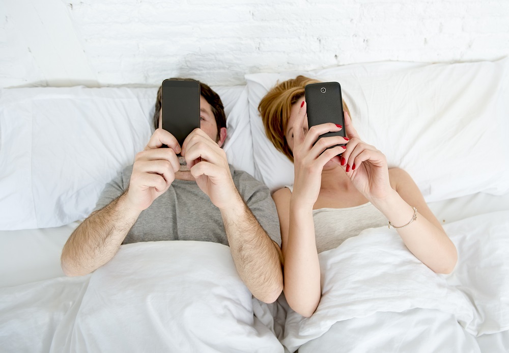 Sennik zdrada. Małżeństwo lezące w łóżku i piszące smsy.