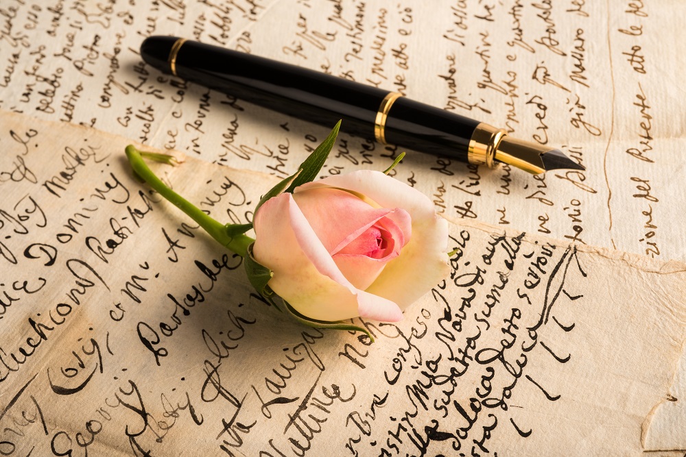 List miłosny, na którym leży pióro i róża.