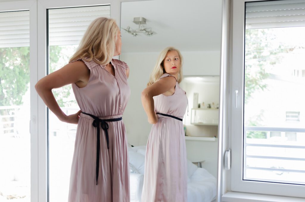 sukienka na wesele dla 50-latki - dojrzała kobieta przegląda się w lustrze