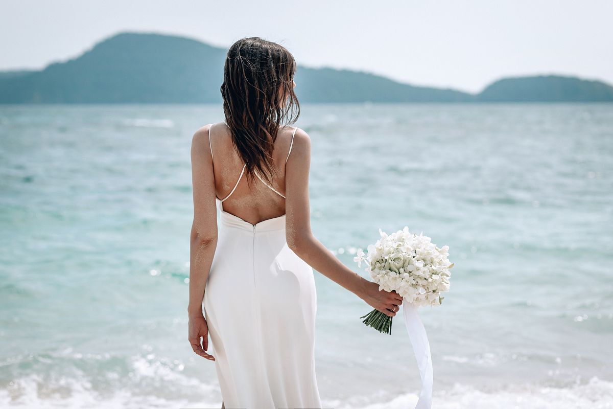 Suknia ślubna odkryte plecy - panna młoda stojąca pod brzegiem morza