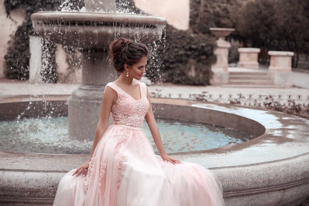 Różowa suknia ślubna. Panna młoda w różowej sukni siedząca na fontannie.