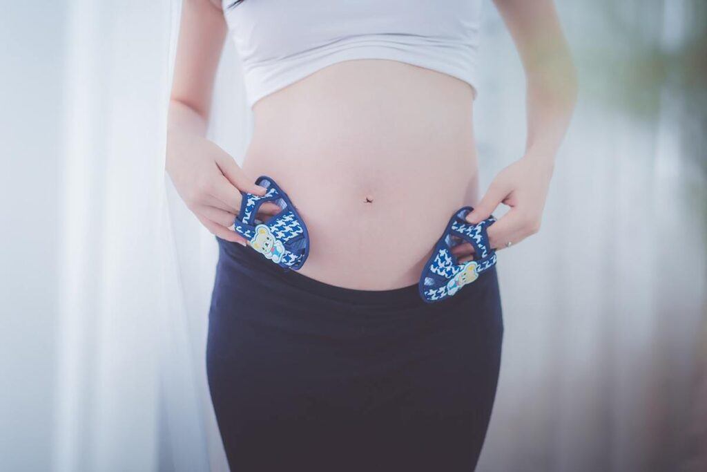 kobieta w ciąży podczas ćwiczeń trzyma małe buciki