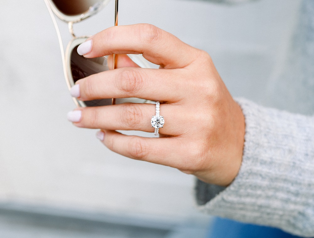 na którym palcu nosi się pierścionek zaręczynowy - kobieta trzyma okulary słoneczne dłonią z pierścionkiem zaręczynowym