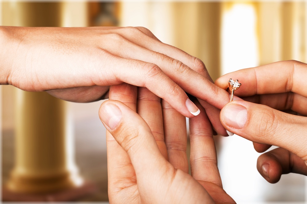 na którym palcu nosi się pierścionek zaręczynowy - mężczyzna wkłada pierścionek zaręczynowy na prawą dłoń kobiety