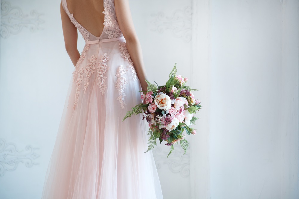 Różowa suknia ślubna. Panna młoda w różowej sukni trzymająca bukiet kwiatów.