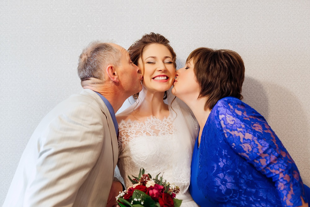 życzenia ślubne - rodzice całują panną młoda w policzek