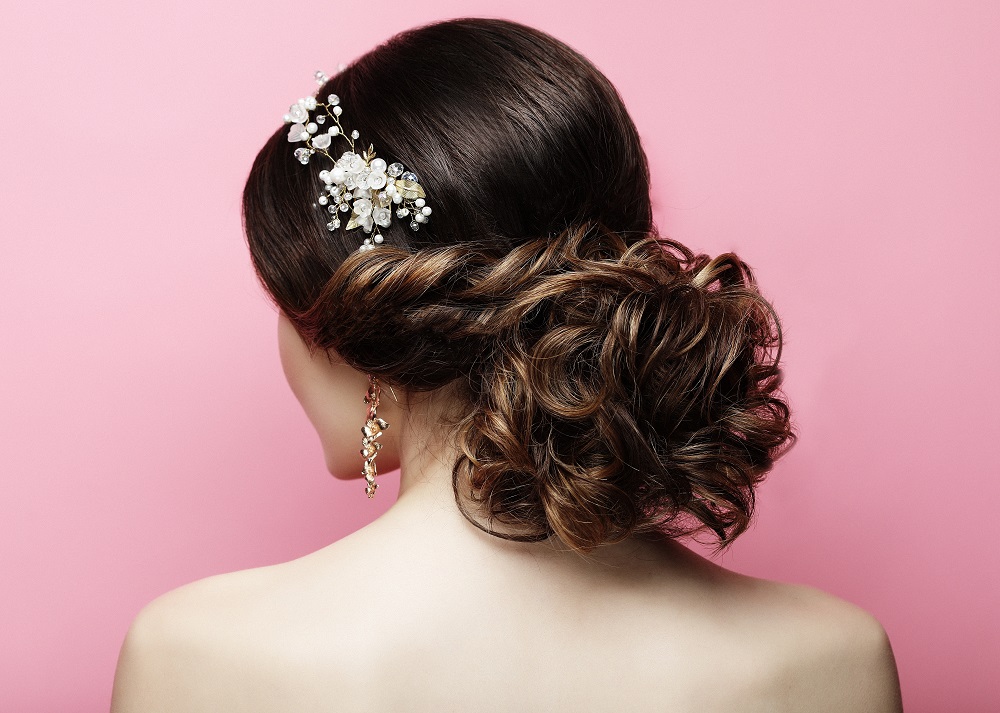 Ciemne włosy spięte w delikatny kok na linii szyi jako przykład fryzury na wesele.