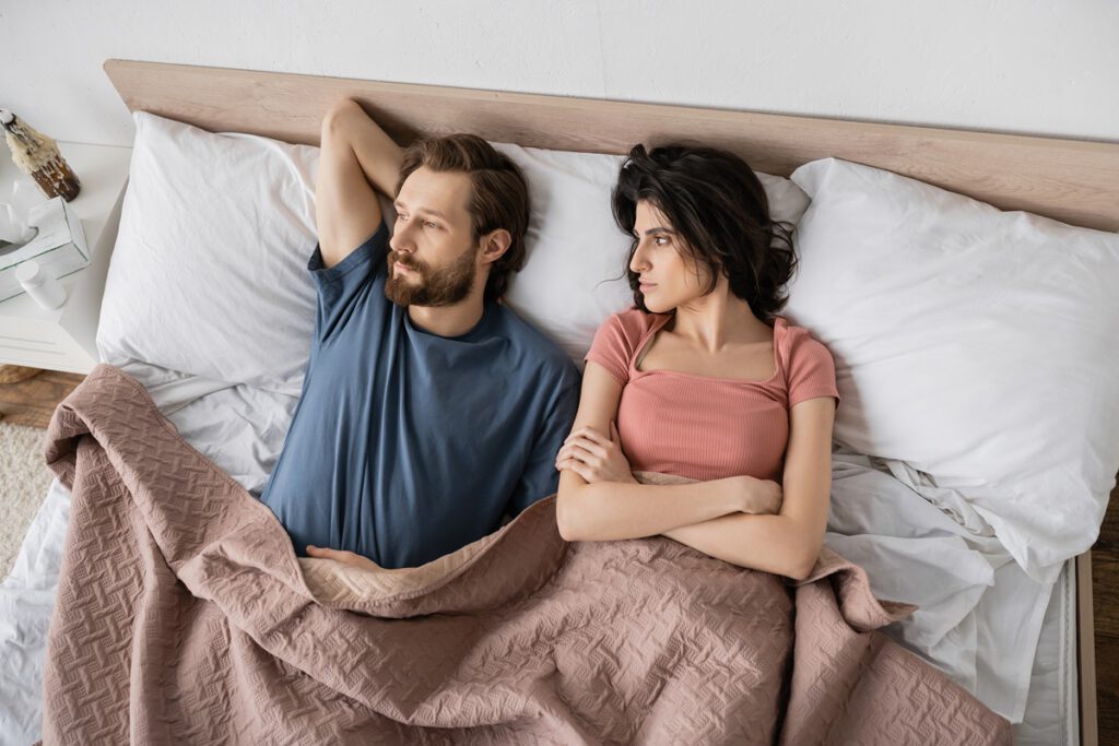 Pokłócona para leży w łóżku i rozmawia, czy sen wskazuje na zdradę

