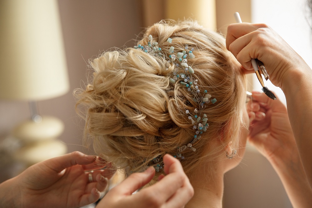Piękny kok na blond włosach z ozdobą z kamyczków jako przykład fryzury na wesele.