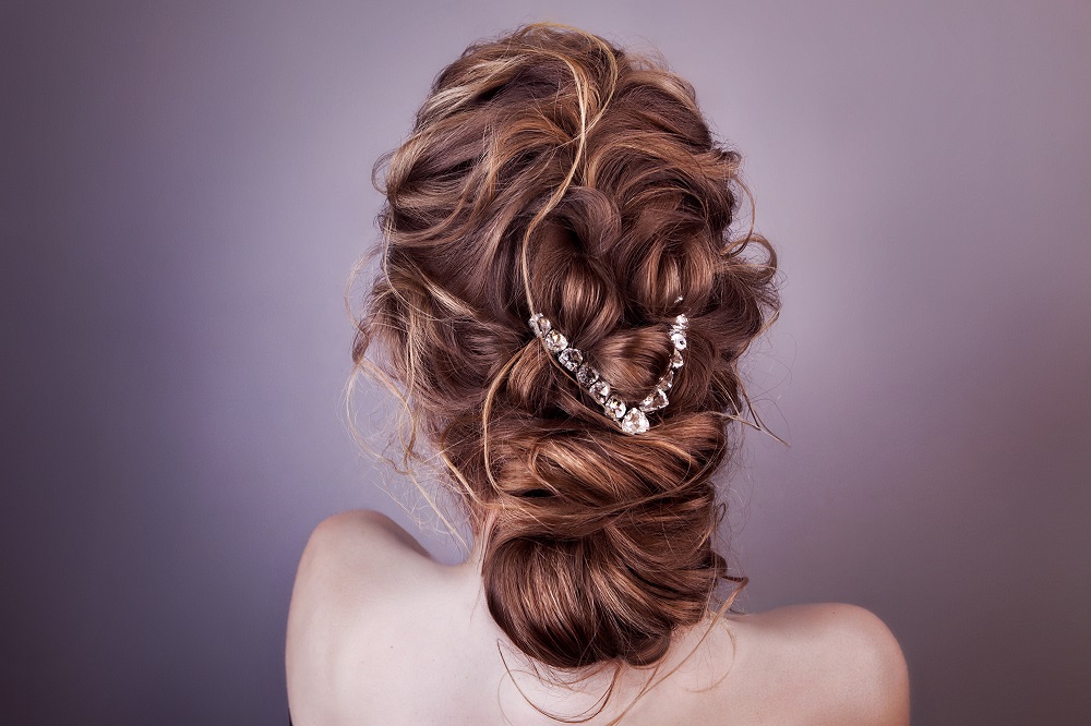 Piękne upięcie na długich brązowych włosach z ozdobą z diamentów jako przykład fryzury na wesele.