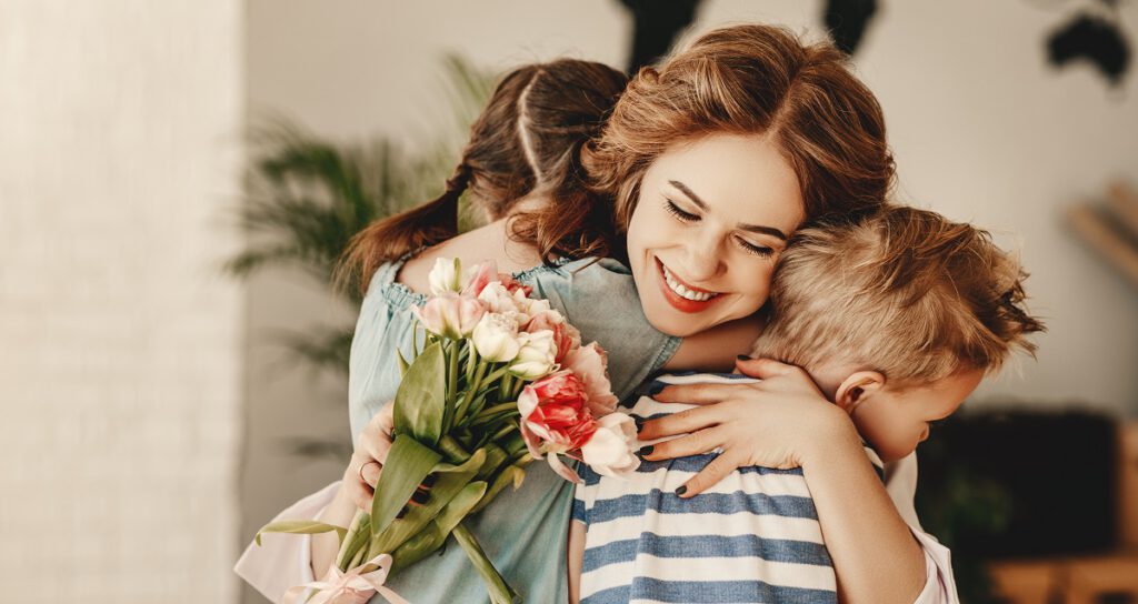 prezent na dzień matki-dzieci przytulają mamę, która trzyma kwiaty