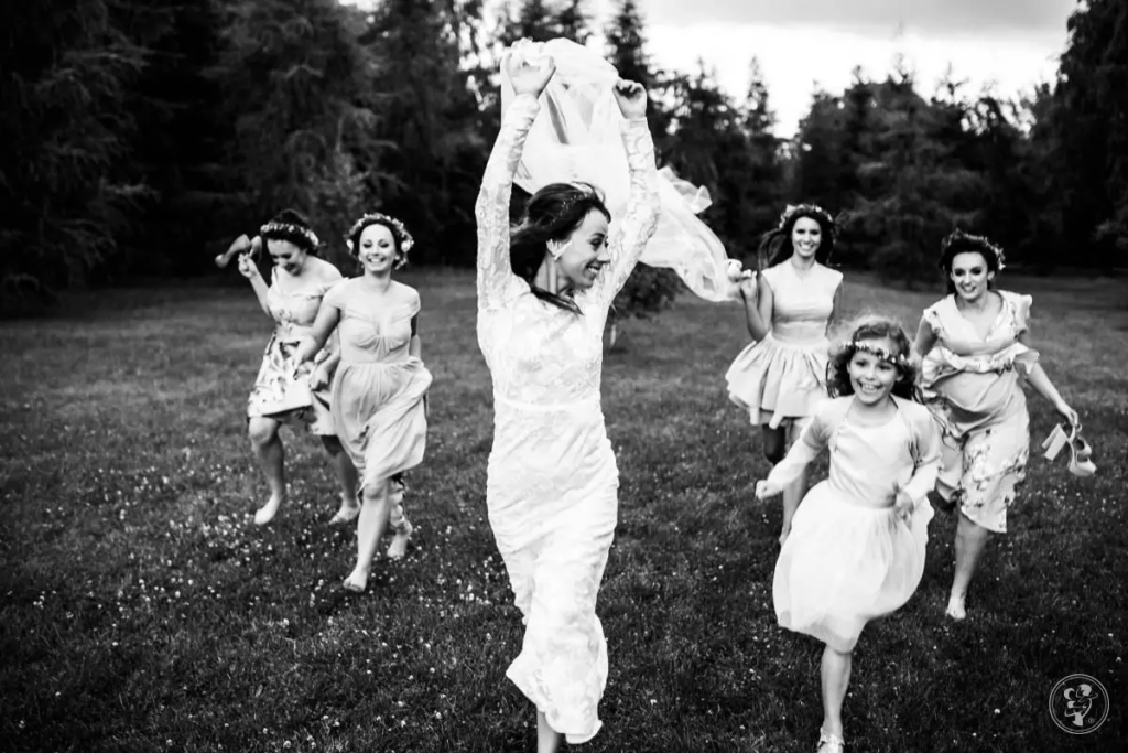 Czarno-białe zdjęcie panny młodej biegnącej wraz z druhnami