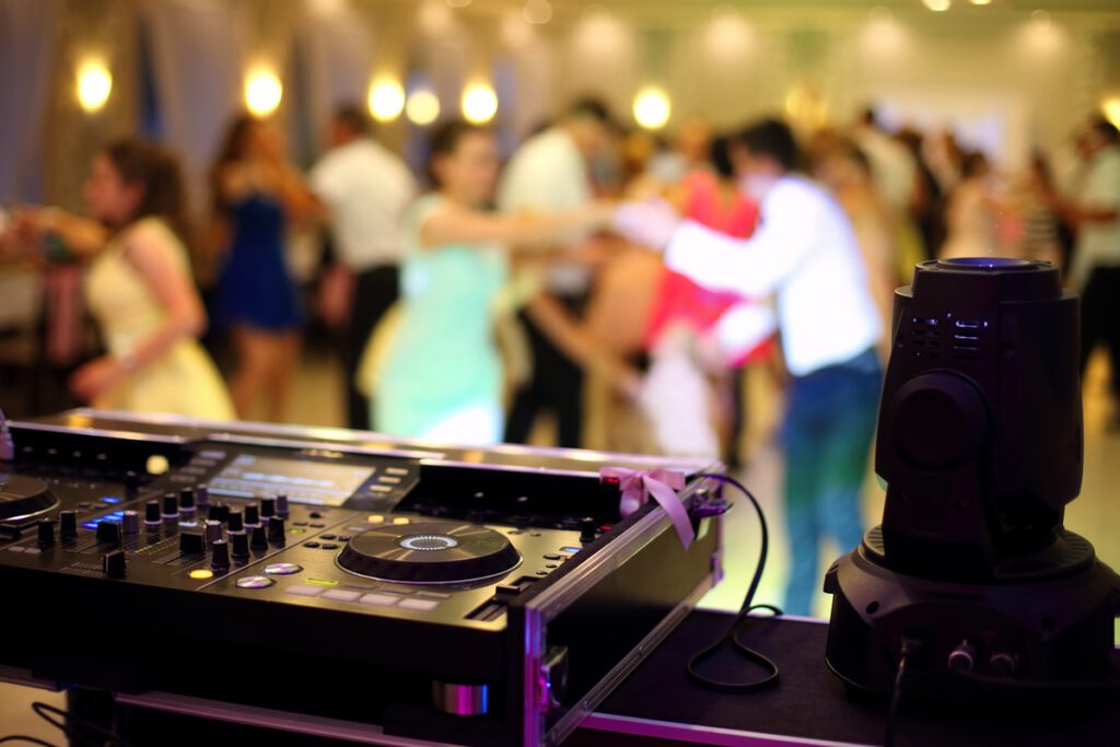 Konsola DJ-a, w tle bawiący się goście do piosenek weselnych