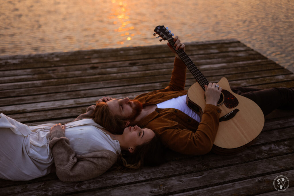 Życzenia na rocznicę ślubu - mężczyzna z gitarą i kobieta leżący na pomoście nad jeziorem