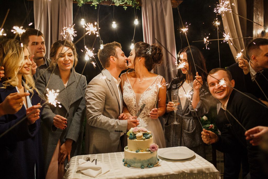 Atrakcje na wesele - para młoda krojąca tort wśród gości z zimnymi ogniami